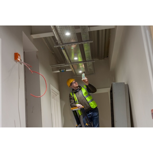 STANLEY FMHT77653-0 detector used by worker in safety vest under ceiling wiring, indoor photography.