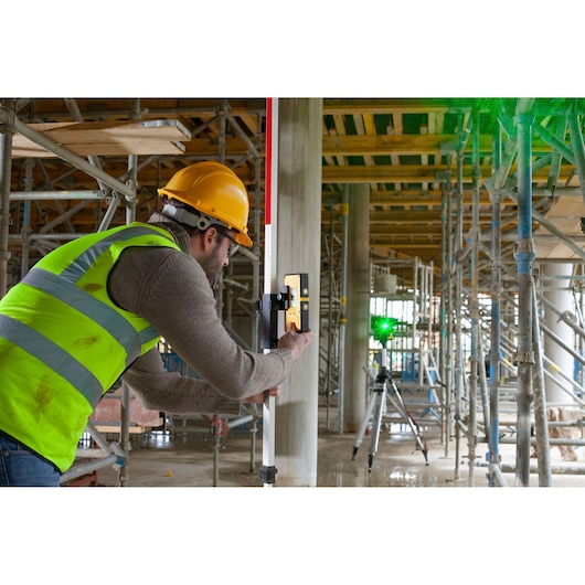 STANLEY FMHT77653-0 laser receiver used on construction site with scaffolding and worker in safety gear.