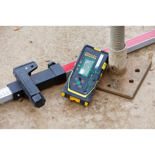 Stanley FMHT77653-0 laser receiver shown on construction site with level rod and base plate.