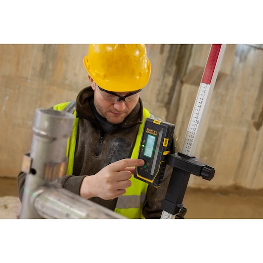 Photo of STANLEY FMHT77653-0 laser receiver mounted on a measuring rod, operated by a worker on construction site.