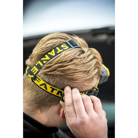 STANLEY FMHT81509-0 headlamp with yellow and black adjustable strap worn on head, close-up side view.