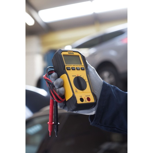 STANLEY FMHT82563-0 smart digital multimeter handheld, yellow and black, with probes in an automotive setting.