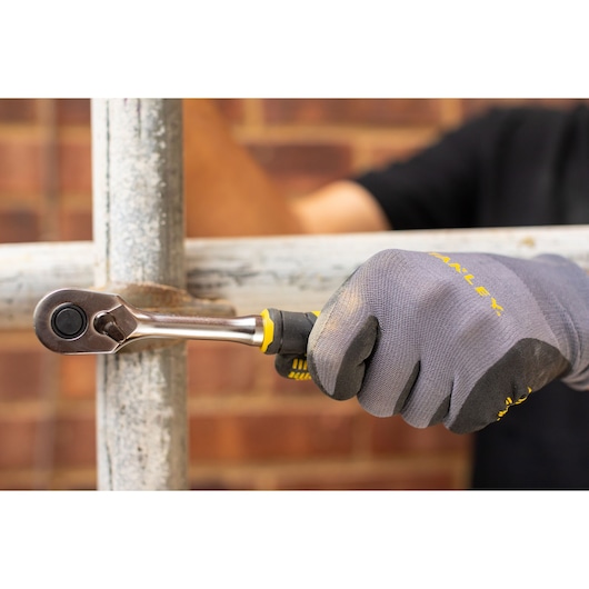 STANLEY FMMT82677-0 ratchet wrench used on metal pipe, close-up, gloved hand holding handle.