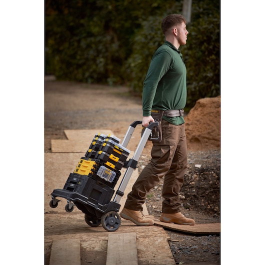 Photo of STANLEY FMMT98102-0 toolboxes stacked on a rolling trolley outdoors, pulled by a person in workwear.