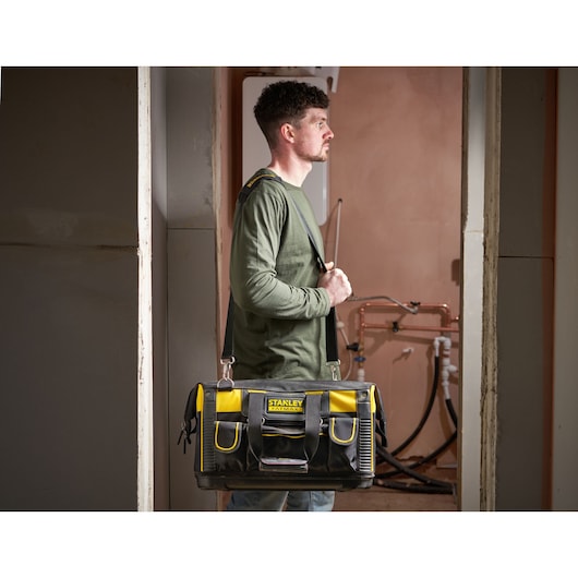 STANLEY FMST1-71180 tool bag with shoulder strap, black and yellow, carried by a person in a work setting.