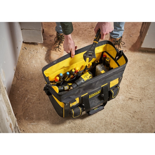 STANLEY FMST1-71180 tool bag filled with hand tools and accessories, top view, on construction site floor.