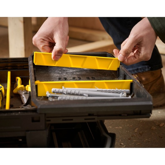 Close-up of a person organizing a Stanley toolbox tray with yellow dividers, containing screws and dowels.