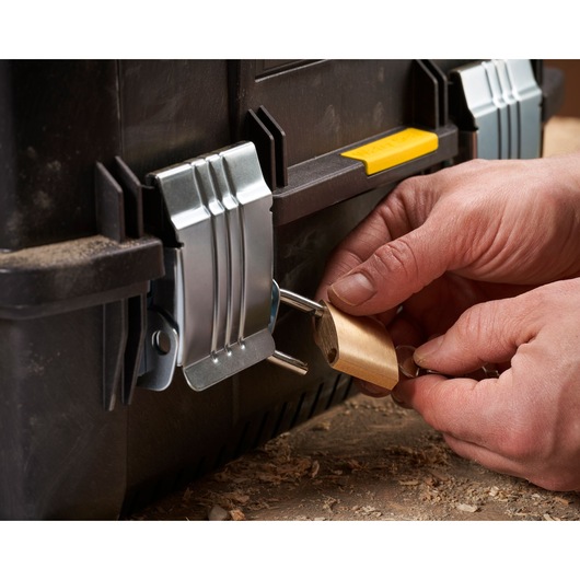Close-up of hands locking a black toolbox with a metal latch and a brass padlock.