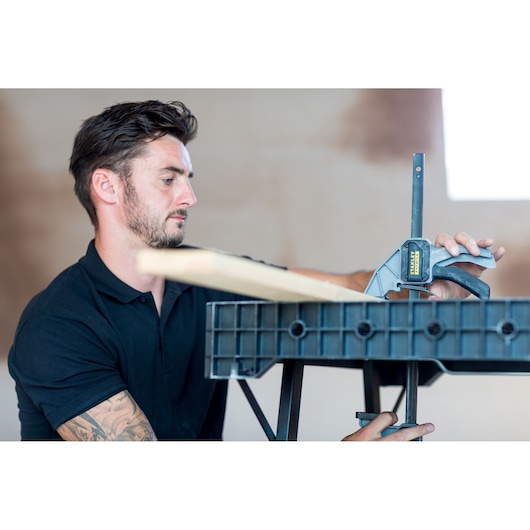 Stanley FMST1-75672 clamp securing wood on black workbench in workshop setting.
