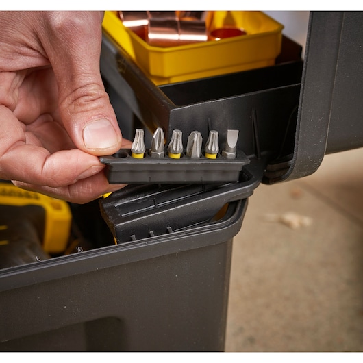 A close-up of a hand holding a set of screwdriver bits inside a black Stanley tool box with a yellow organizer tray.