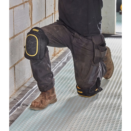 STANLEY FMST82962-1 knee pads, black with yellow trim, worn by worker kneeling on construction site.
