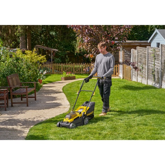 STANLEY SCMWP3401M1-XE lawn mower in use on grass in a garden setting, side angle.
