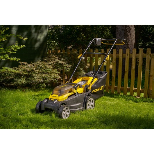 STANLEY SCMWP3401M1-XE lawn mower with yellow and black body on green lawn, photographed outdoors.