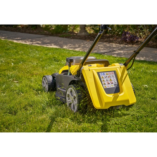 Photo of STANLEY SCMWP3701M2 lawn mower side view on grass with yellow and black body and large rear wheels.