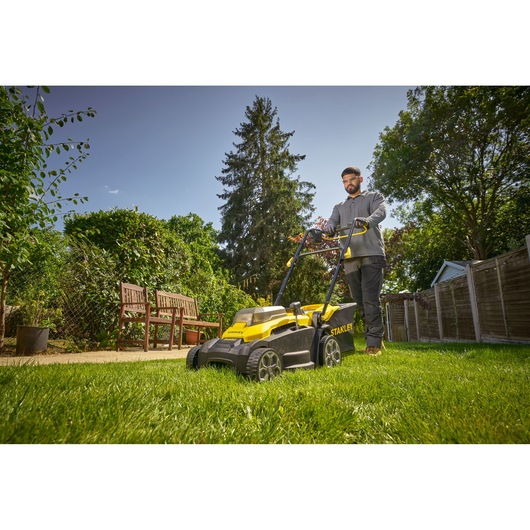 Photo of STANLEY SCMWP3701M2 lawn mower in use on grass in a garden setting, yellow and black design visible.