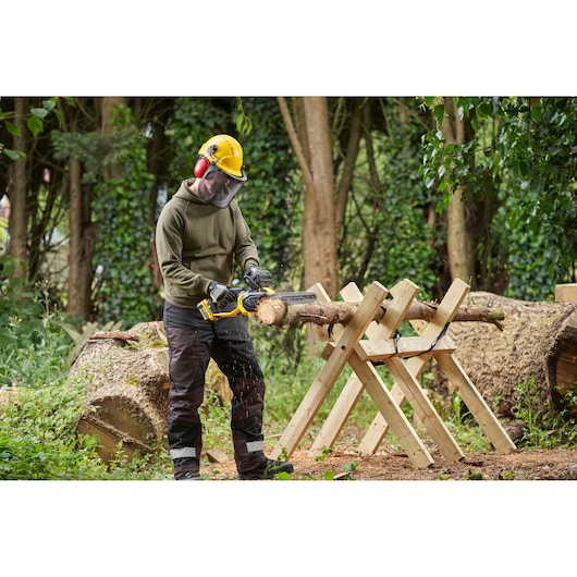 STANLEY SFMCCS730M1 chainsaw in use cutting a log outdoors with operator wearing safety gear.