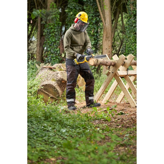 STANLEY SFMCCS730M1 chainsaw in use outdoors cutting wood, shown held by a person wearing safety gear.