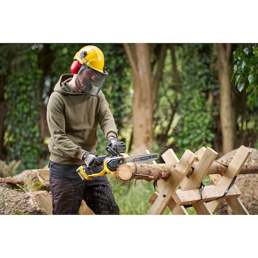 STANLEY SFMCCS730M1 chainsaw in use outdoors, cutting wood on sawhorse, yellow and black tool, photo.