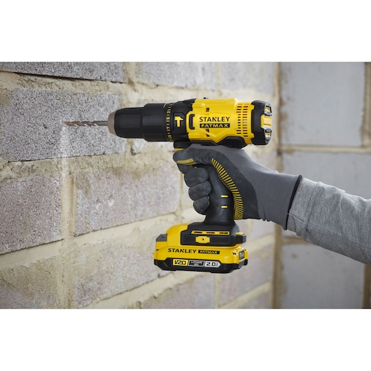 STANLEY SFMCD711D11 cordless drill, yellow and black, in use drilling brick wall.