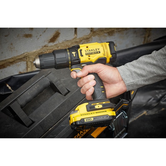 STANLEY SFMCD711D21 cordless drill, yellow and black, held in hand, side angle, tool box in background.