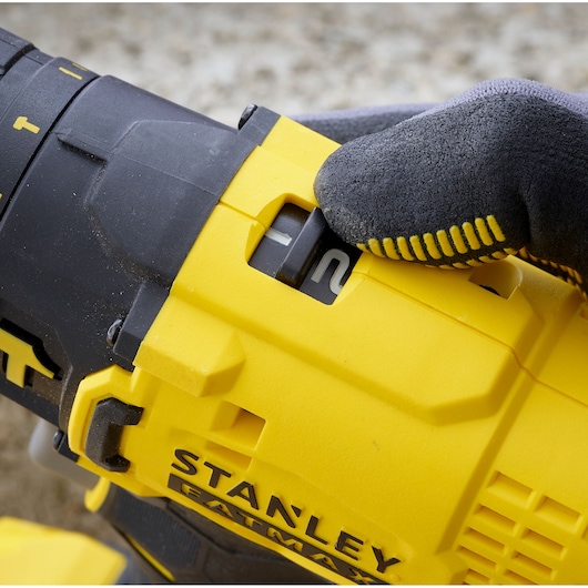 Photo of STANLEY SFMCD711D21 drill with gloved hand adjusting speed setting, close-up side angle.