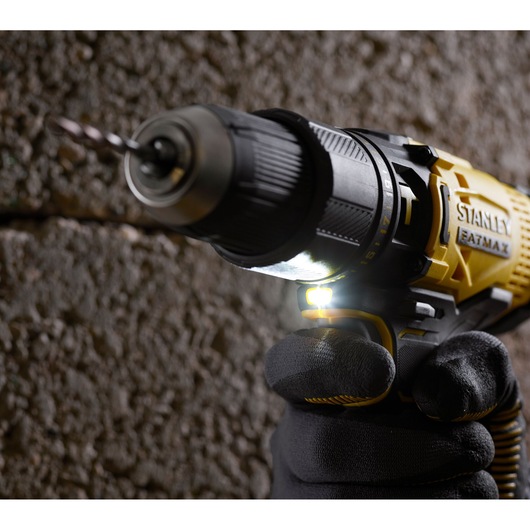 STANLEY SFMCD711D21 cordless drill in use close-up, yellow and black, drilling into concrete wall.