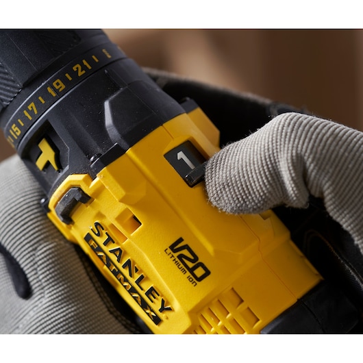 Photo of STANLEY SFMCD711D21 V20 cordless drill close-up, yellow casing, gloved hand adjusting settings.