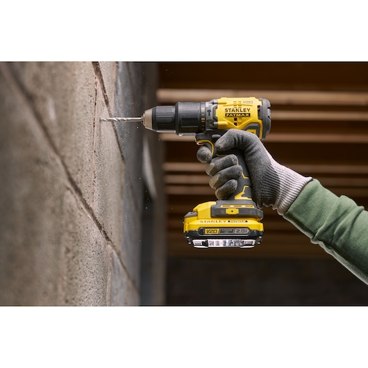 STANLEY SFMCD715D1K cordless drill in use, drilling into a concrete wall, side view, yellow and black design.