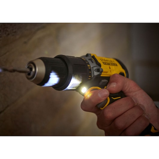 STANLEY SFMCD715D1K drill in use, close-up showing LED light and yellow-black body against a wall.