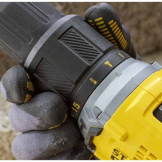 STANLEY SFMCD715D1K drill close-up, gloved hand adjusting torque setting, yellow and black body.