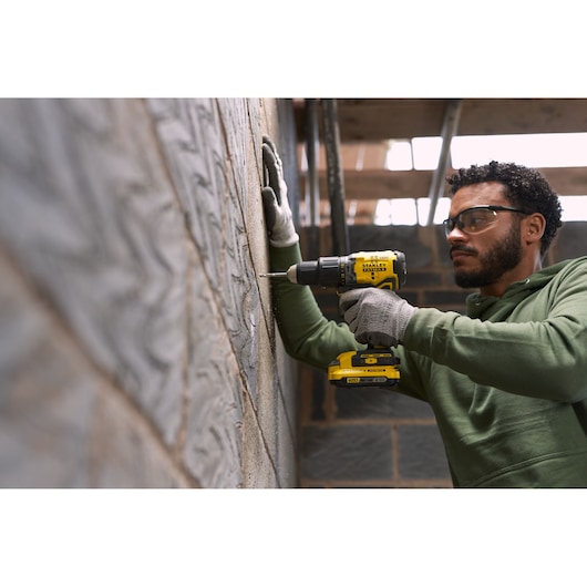 Stanley SFMCD715D2K cordless drill in use drilling into concrete wall, construction context, side angle.