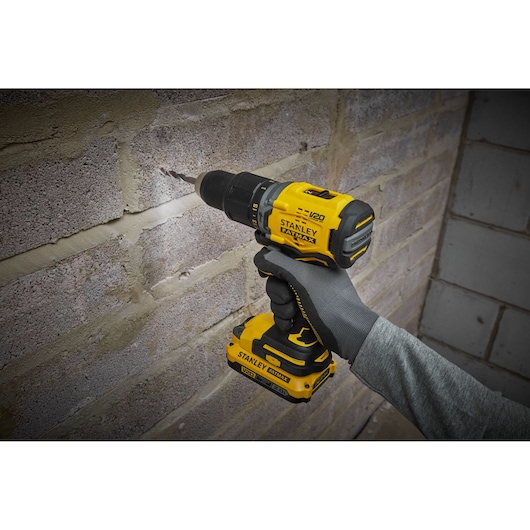 STANLEY SFMCD715D2K cordless drill in use drilling into a brick wall, shown in a close-up side angle.