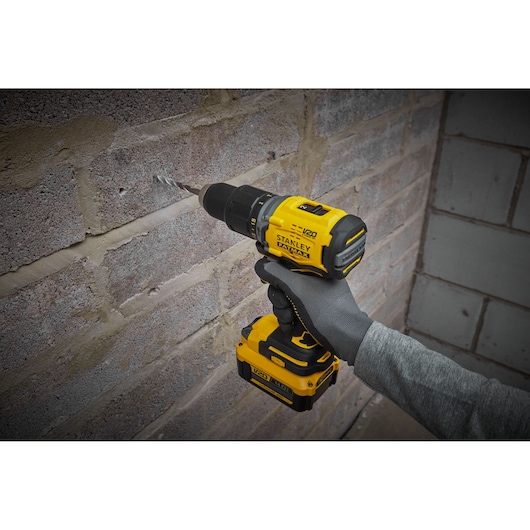 Stanley SFMCD715M12 cordless drill in use on brick wall, yellow and black design, close-up view.