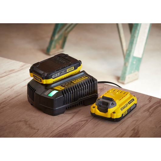 STANLEY SFMCD715M12 battery charger and battery, yellow and black, on wooden surface, side angle.