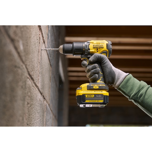 STANLEY SFMCD715M12 cordless drill in use on a concrete wall, close-up of gloved hand holding yellow power tool.