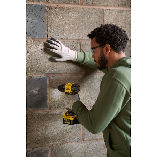 Photo of STANLEY SFMCD715M12 cordless drill in use against a brick wall, user wearing gloves and green jacket.