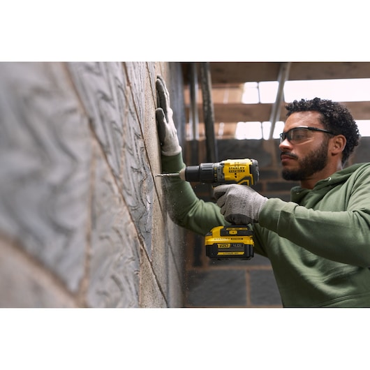 Photo of STANLEY SFMCD715M12 cordless drill in use, drilling into a concrete wall, product held by person wearing gloves.