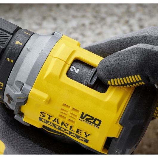 Photo of STANLEY SFMCD715M12 drill close-up, yellow casing, gloved hand switching speed setting.