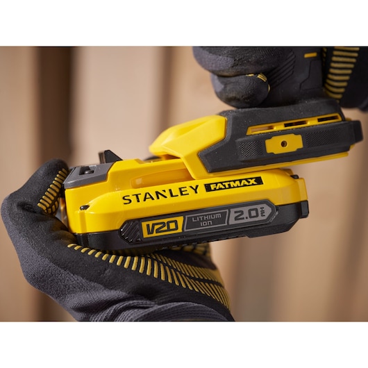 STANLEY SFMCD750B power tool held in gloved hands, highlighting yellow V20 FATMAX 2.0Ah lithium-ion battery.