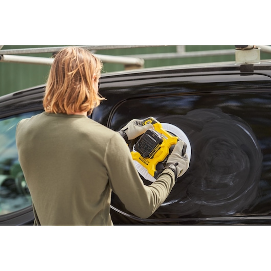Photo of STANLEY SFMCE100D2 polisher being used on a black vehicle surface outdoors.
