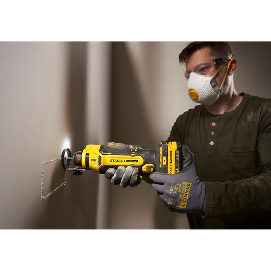 Photo of STANLEY SFMCE200B rotary tool cutting drywall, tool held by gloved hands, jobsite setting.