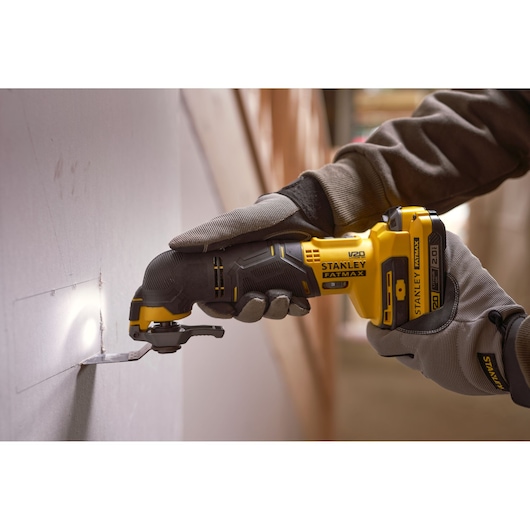 STANLEY SFMCE500D2K oscillating multi-tool cutting drywall, close-up side angle, yellow and black tool.