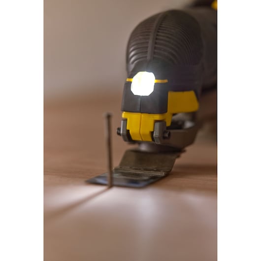 STANLEY SFMCE500M1K oscillating multi-tool close-up with LED light on, cutting near a nail on wood surface.