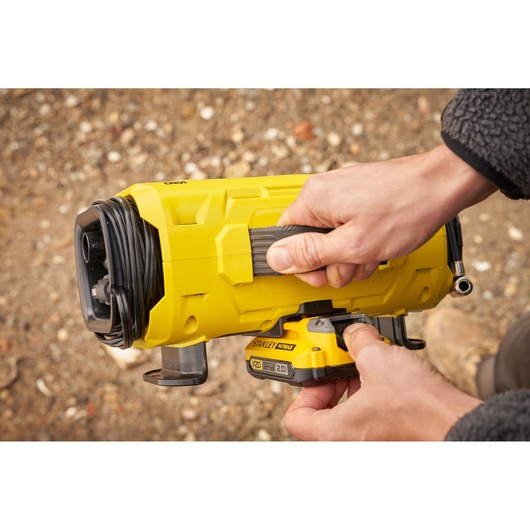Photo of STANLEY SFMCE520B battery-powered compressor with yellow casing, shown being held and operated outdoors.