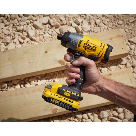 Photo of a STANLEY SFMCF800C2K cordless impact driver held in hand, yellow and black, outdoors on wood boards.