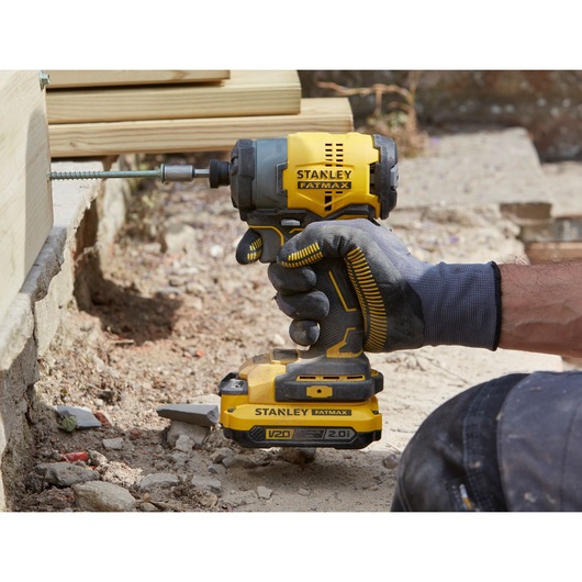 Stanley SFMCF810D1K impact driver in use outdoors, yellow and black design, worker wearing gloves.
