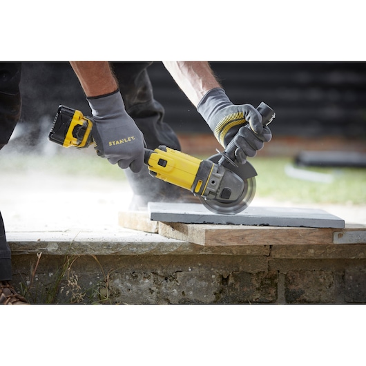 STANLEY SFMCG400B cordless angle grinder in use cutting a concrete slab outdoors.