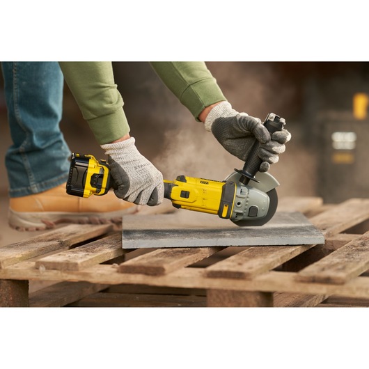 STANLEY SFMCG400M1K angle grinder in use cutting tile, yellow and black tool on wooden pallet outdoors.