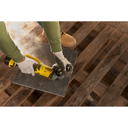 STANLEY SFMCG400M1K cordless angle grinder in use cutting tile, worker wearing gloves and safety boots.