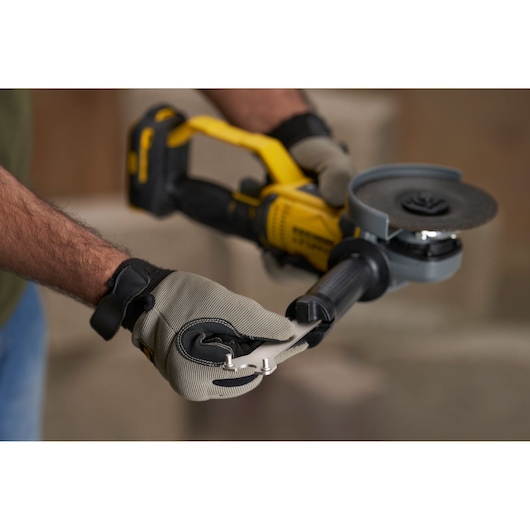 STANLEY SFMCG400M1K angle grinder held by gloved hands with adjustment tool, close-up photo.